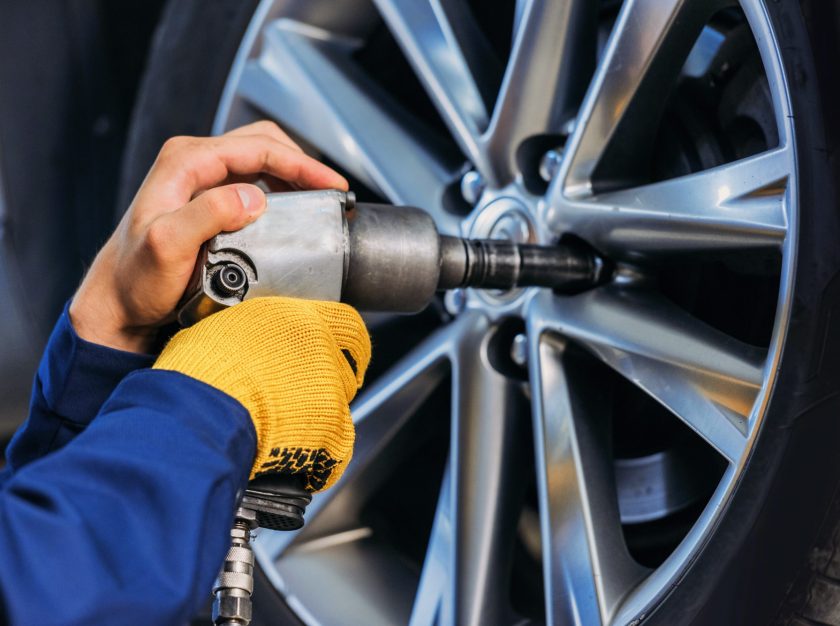 Eine Hand mit Schlagschrauber löst an einer silbernen Autofelge Radmuttern im Reifenservice in der Werkstatt.