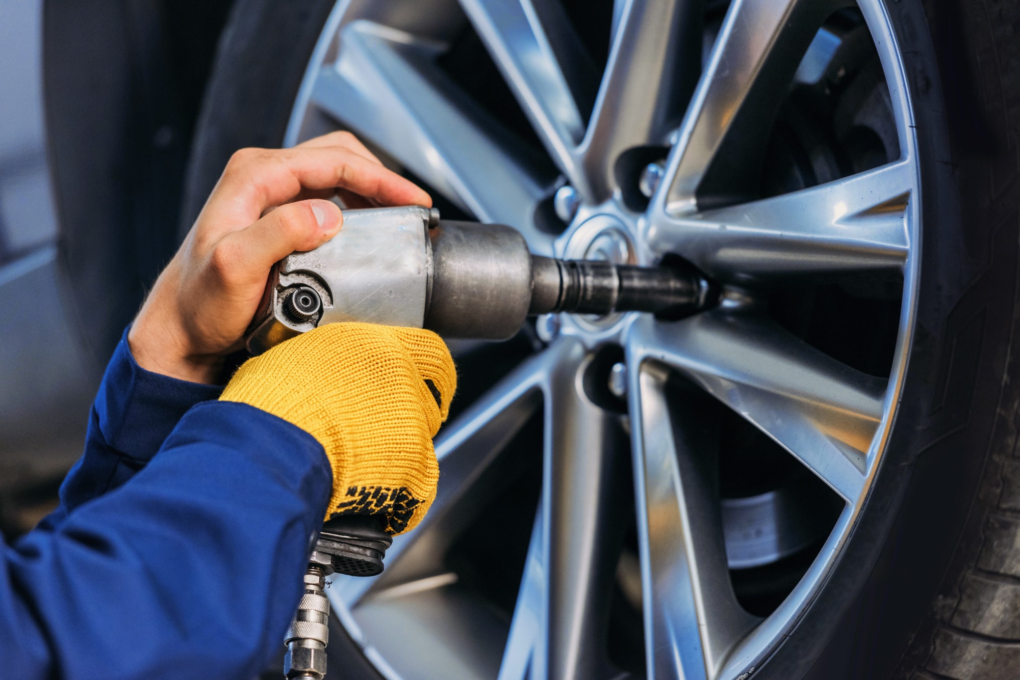 Eine Hand mit Schlagschrauber löst an einer silbernen Autofelge Radmuttern im Reifenservice in der Werkstatt.