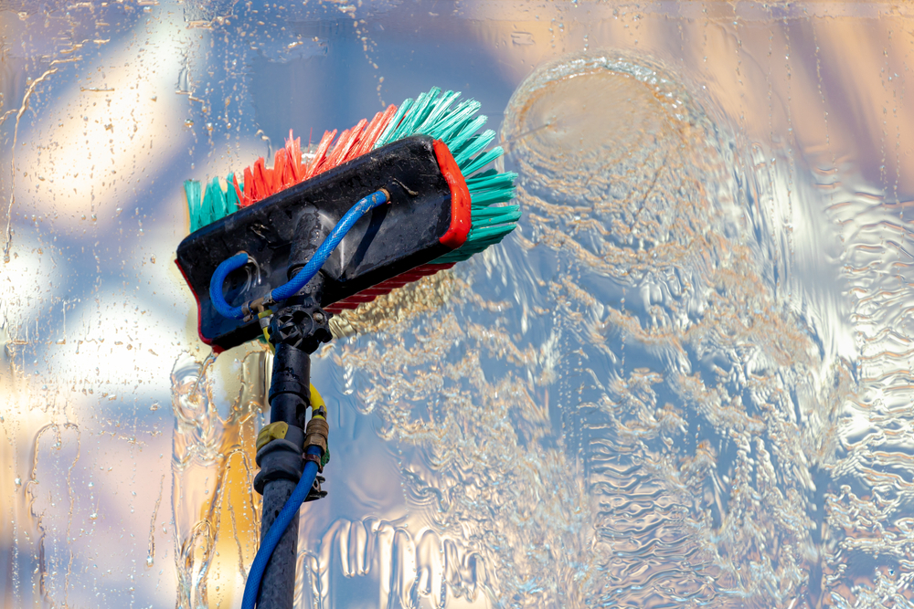 Eine Teleskopbürste entfernt mit Wasser Schmutz und Ablagerungen von einer Glasfläche bei der professionellen Glasreinigung.